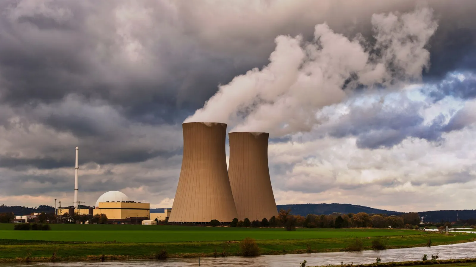 Centrale nucléaire : deux tours de refroidissement en panache et bâtiment réacteur à dôme, sous un ciel chargé