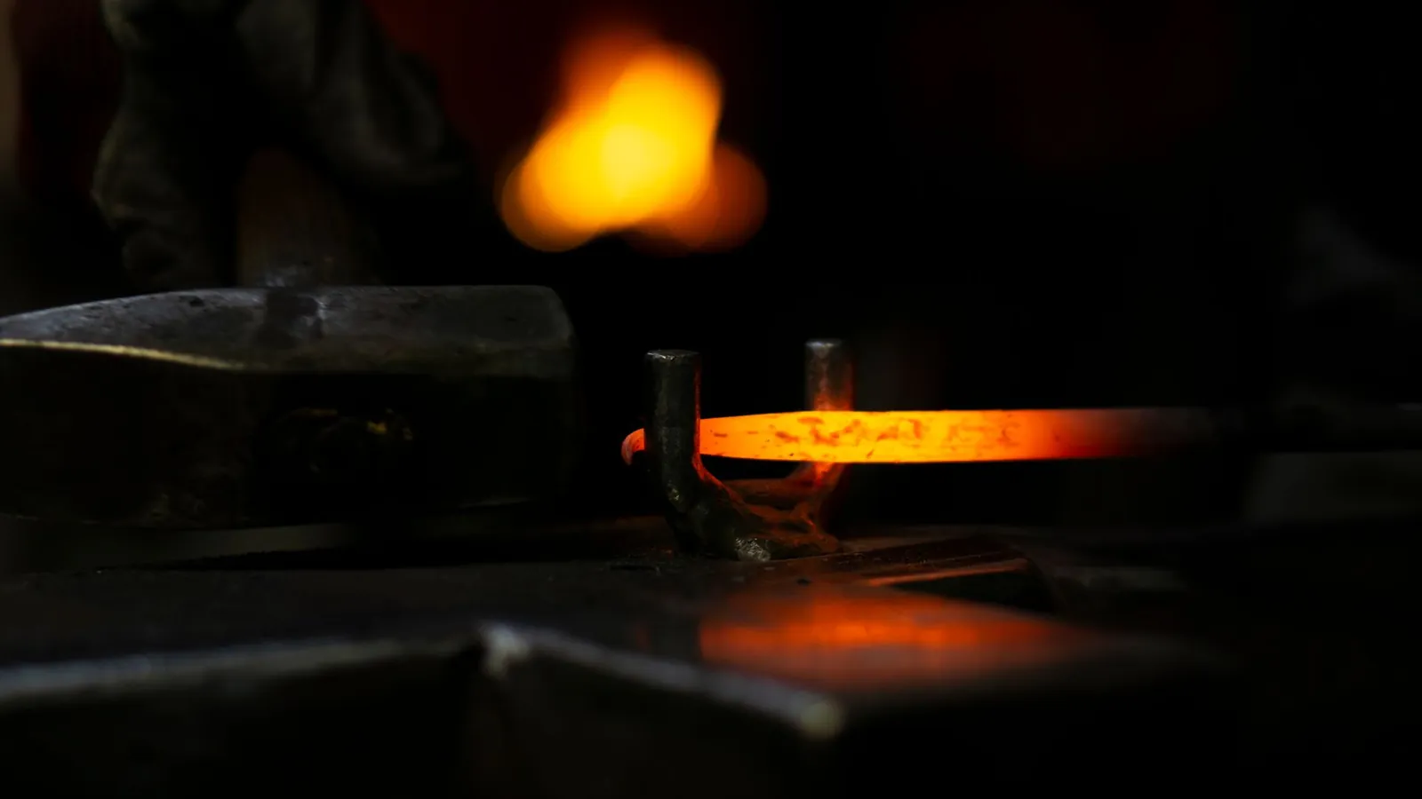 Barre d'acier incandescente posée sur l'enclume, le foyer de la forge rougeoyant à l'arrière-plan