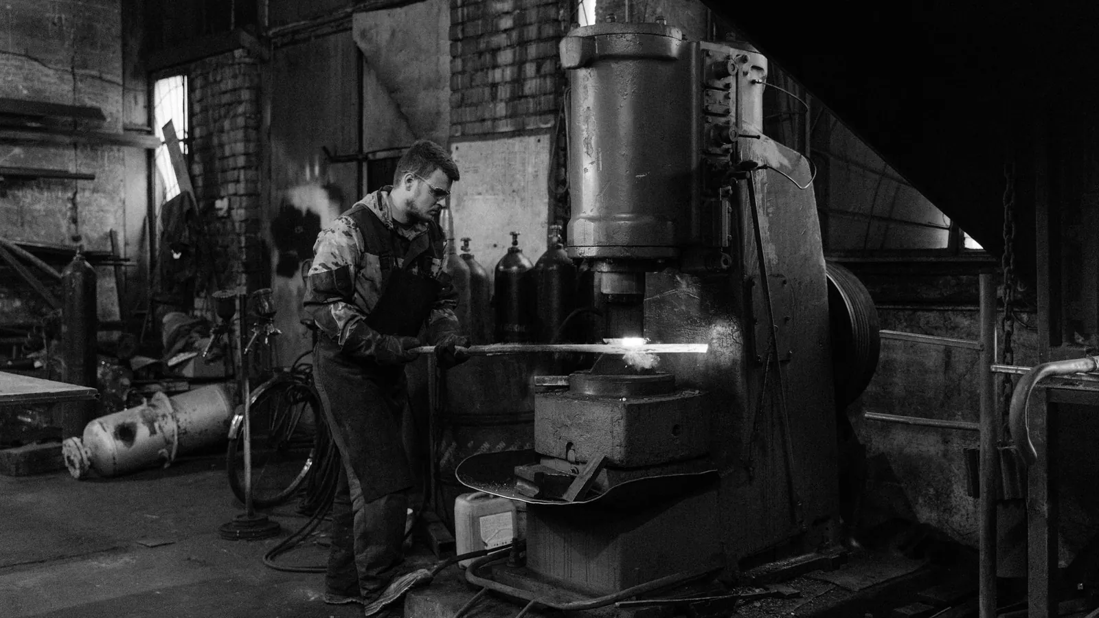 Forgeron engageant une barre chauffée sous un marteau-pilon, photographie en noir et blanc